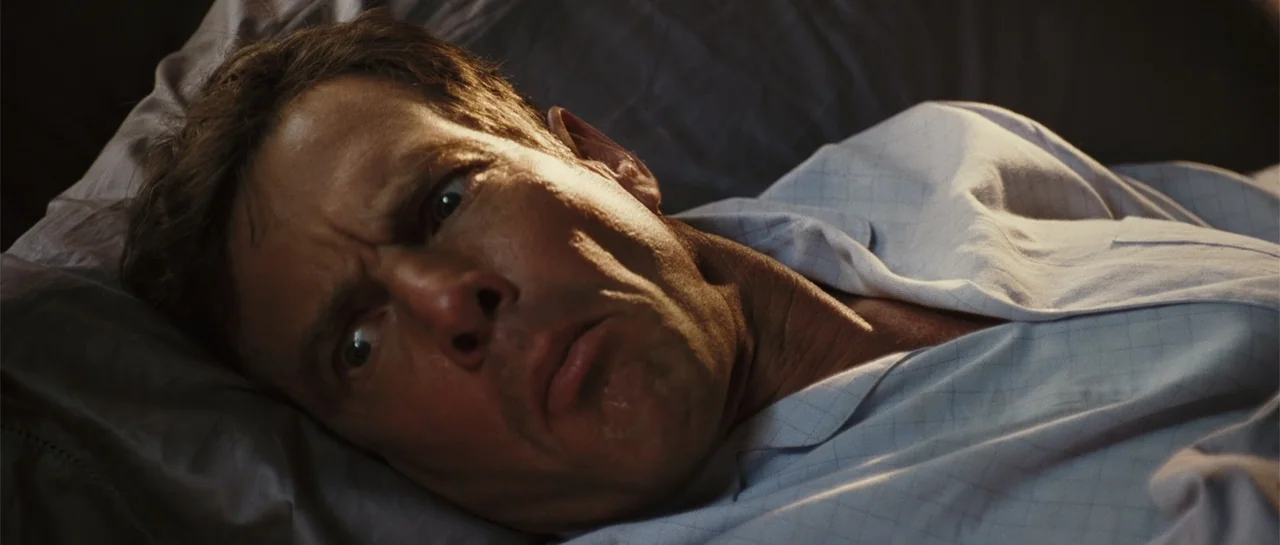 Yours, Mine & Ours (2005) movie still: closeup — A man lies in bed against a plain grey pillow and bedding. The man turns his head to gaze…