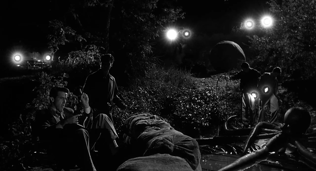 Ed Wood (1994) movie still: wide — A dark outdoor field at night features scattered men investigating a central mysterious object. Multiple bright…