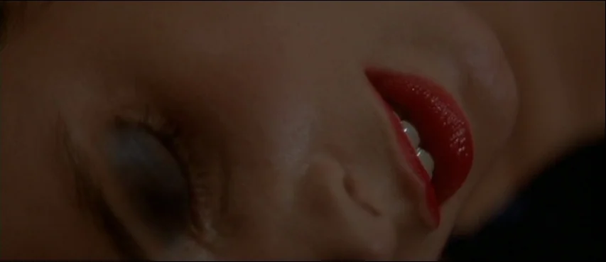 Blue Velvet (1986) movie still: closeup — A close-up view shows a person's lower face with eyes closed and red lips. The background is dark and…