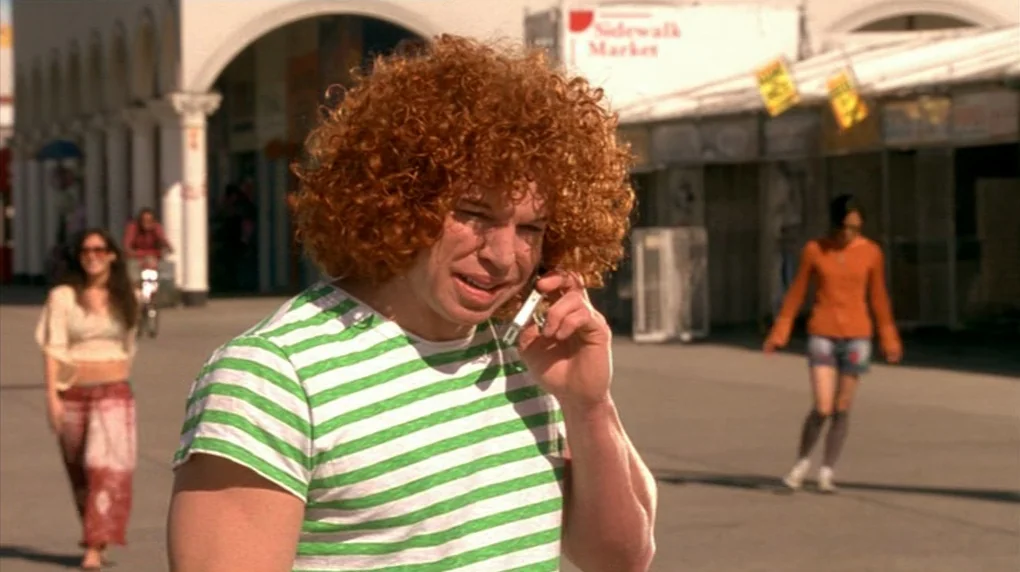 Smiley Face (2007) movie still: medium — A sunny boardwalk area features open store fronts and a pedestrian walkway. A man with curly ginger hair…