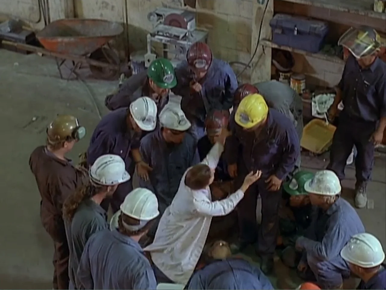 Catch a Falling Star (2000) movie still: wide — An industrial shop floor features concrete walls, metal tools, and a wheelbarrow. A diverse group of…