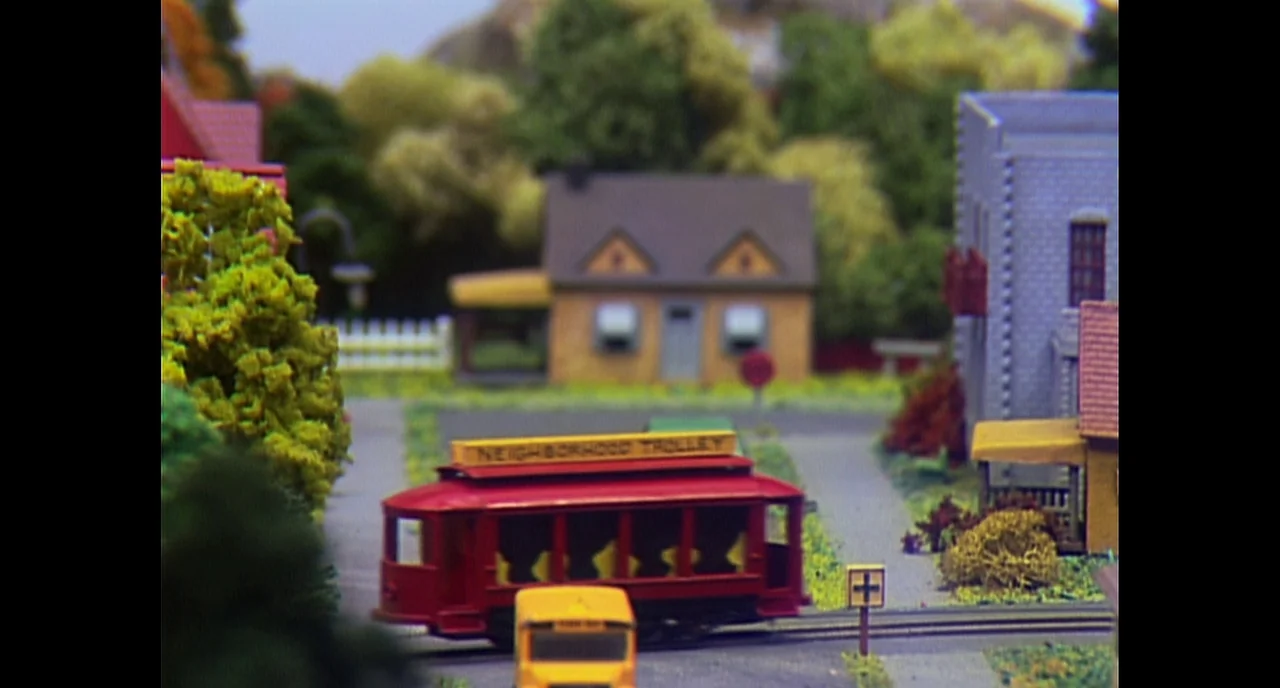 A Beautiful Day In The Neighborhood movie still: wide — A miniature town model with small buildings and trees rendered in scale. A red model trolley…