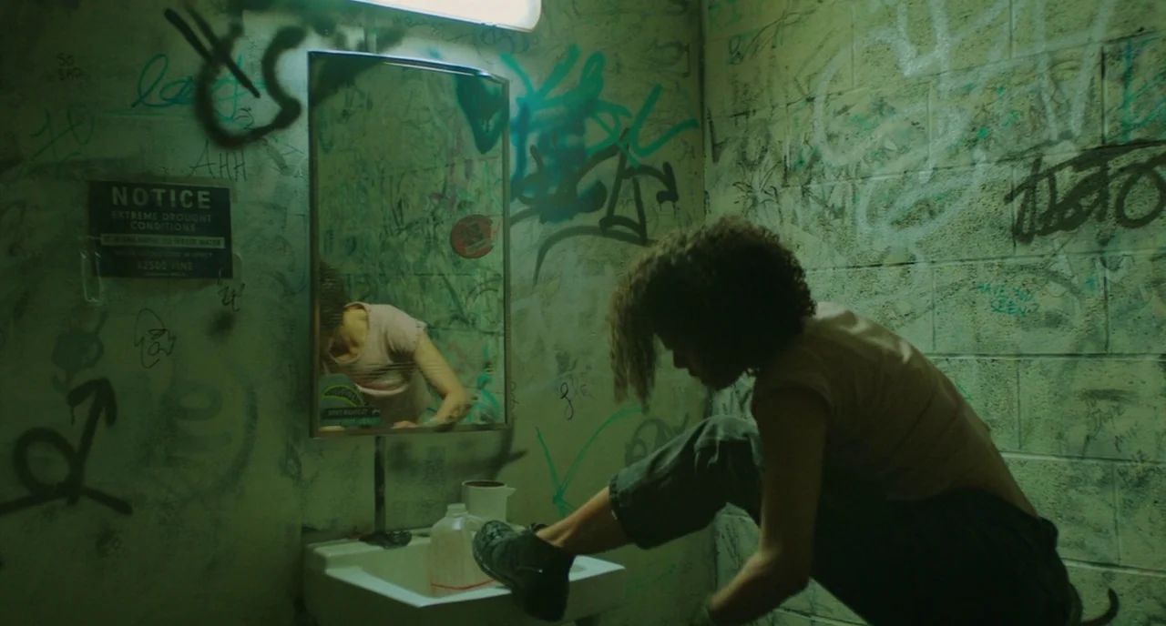 Fast Color (2018) movie still: medium — A grimy public restroom interior features concrete block walls covered in extensive dark graffiti. A person…