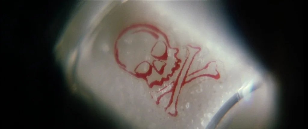 Bringing Out The Dead (1999) movie still: closeup — A glass vial with a red skull and crossbones symbol printed on its surface. The background…