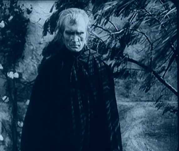 Destiny (1921) movie still: medium — A dark outdoor pathway features dense vegetation and a stark, high-contrast black-and-white look. An elderly…