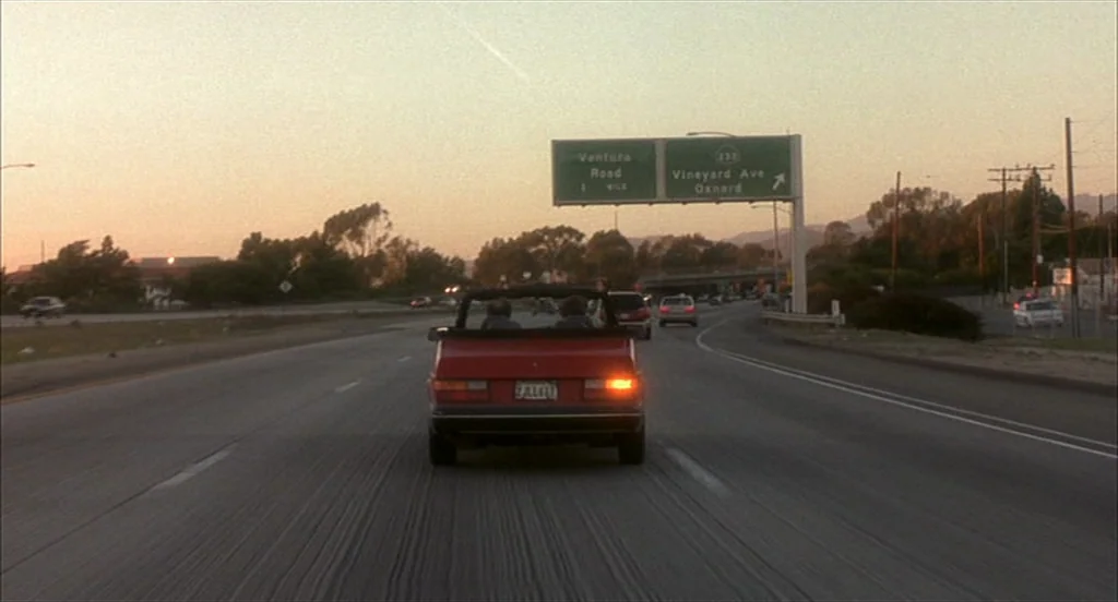Sideways (2004) movie still: wide — A multi-lane highway stretches into the distance during a golden hour sunset. A red convertible drives forward…