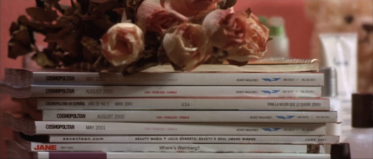 Legally Blonde (2001) movie still: closeup — A stack of various fashion magazines topped with a bouquet of dried pink roses. The magazines are…