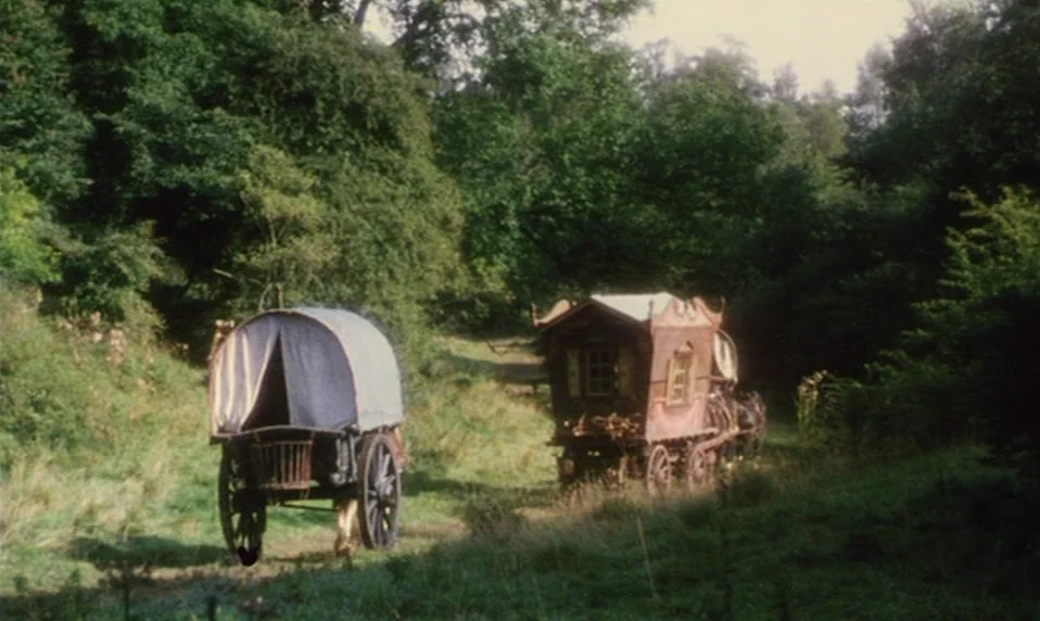 Black Jack (1979) movie still: wide — Two vintage wagons move along a dirt path surrounded by lush, overgrown forest trees. One wagon is a covered…