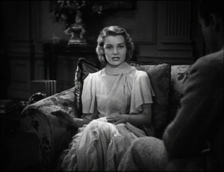 Dracula (1931) movie still: medium — A dimly lit room features a woman seated on a floral patterned sofa. The woman gestures while looking across at…