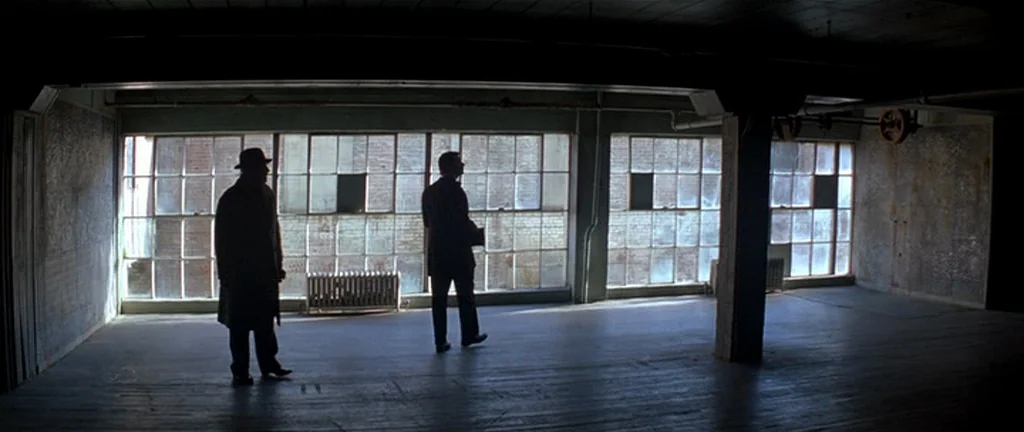 The Prestige (2006) movie still: wide — An empty industrial loft space features large factory windows and exposed support pillars. Two men stand as…