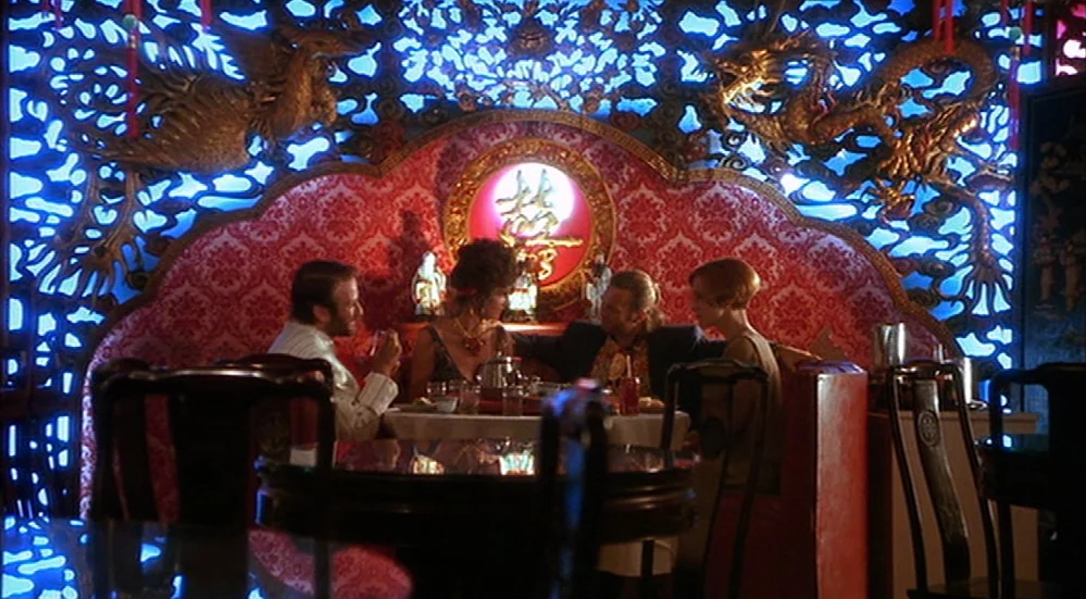 The Fisher King (1991) movie still: medium — A decorated booth in a restaurant features elaborate gold dragon carvings on blue backlighting. Four…