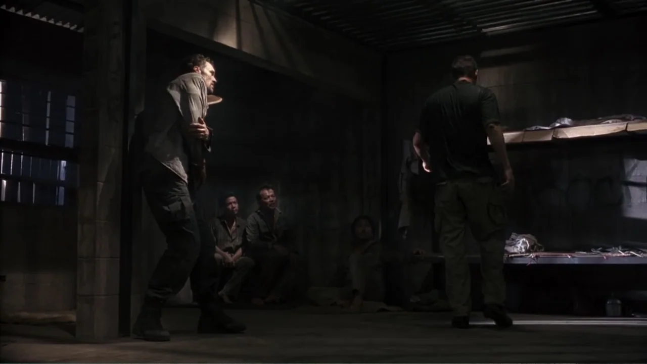 Behind Enemy Lines (2001) movie still: fullbody — A dimly lit concrete room contains metal bunk beds and several men resting. One man stands by a…