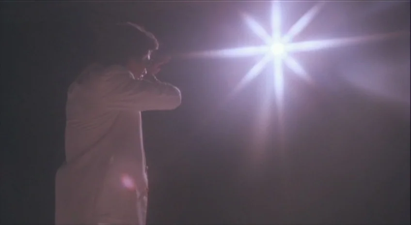 Boxer’s Omen (Mo) (1983) movie still: medium — An indeterminate dark space is filled with a blinding star-shaped light. A man wearing a white jacket…