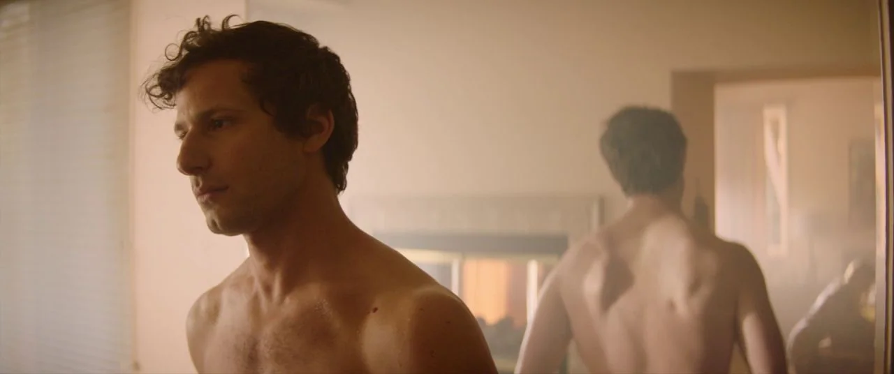 Palm Springs (2020) movie still: medium — A man stands shirtless in a room, his reflection visible in a mirror behind him. The environment is hazy…