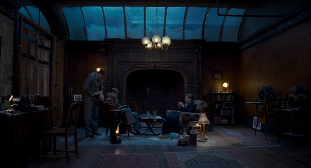 The King’s Speech (2010) movie still: wide — A dimly lit room features a large fireplace, heavy wooden paneling, and a glass ceiling. Three men sit…