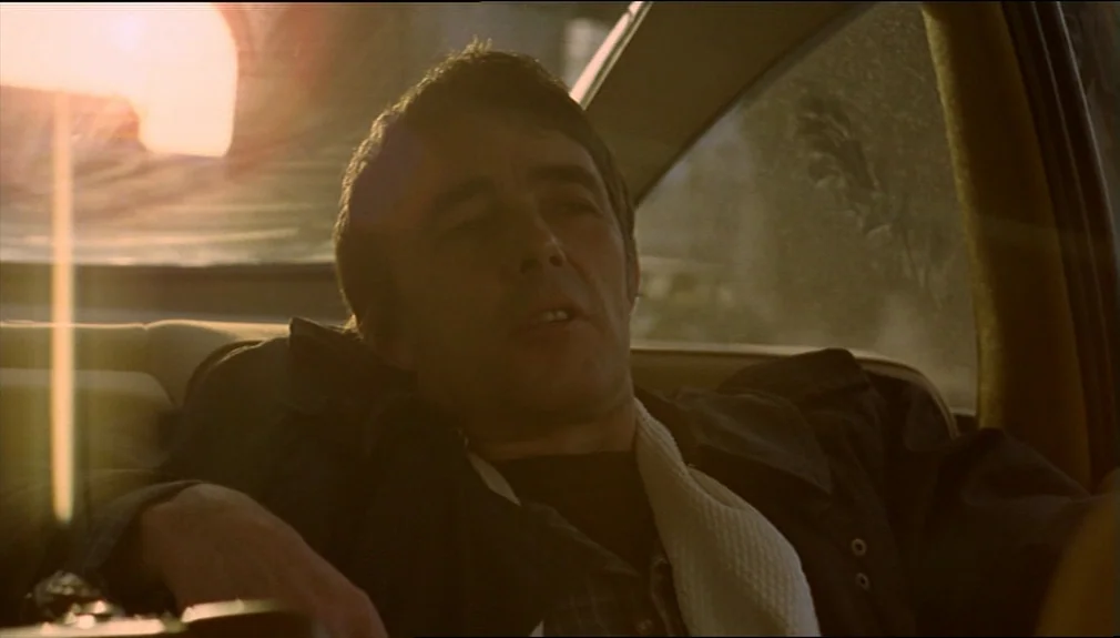 The American Friend (1977) movie still: medium — A man sits in the passenger seat of a vehicle during golden hour light. The sun glows brightly…