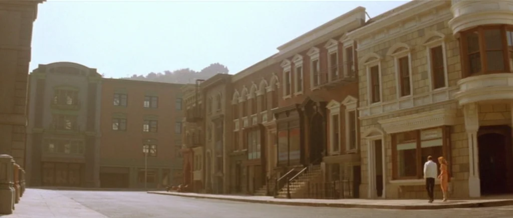 Where The Truth Lies (2005) movie still: wide — A wide view of a quiet, empty urban street lined with multi-story brick buildings. A man and a woman…