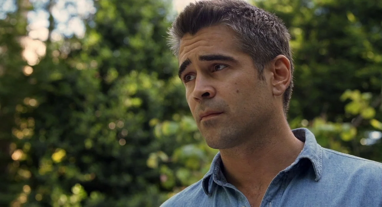 London Boulevard (2010) movie still: closeup — A man stands outdoors in front of a dense wall of out-of-focus green leaves. He looks away from the…