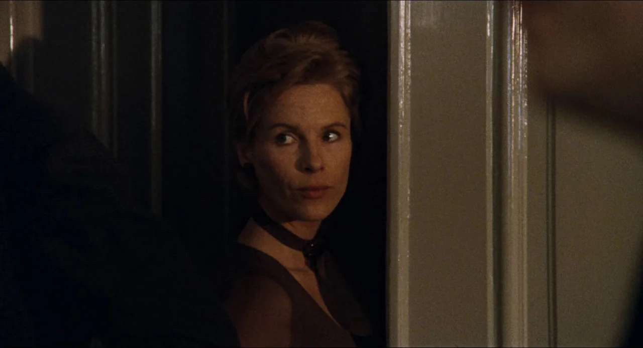 The Touch (1971) movie still: closeup — A woman stands in a shadowed doorway of a dimly lit interior room. She gazes off-camera to the left while…