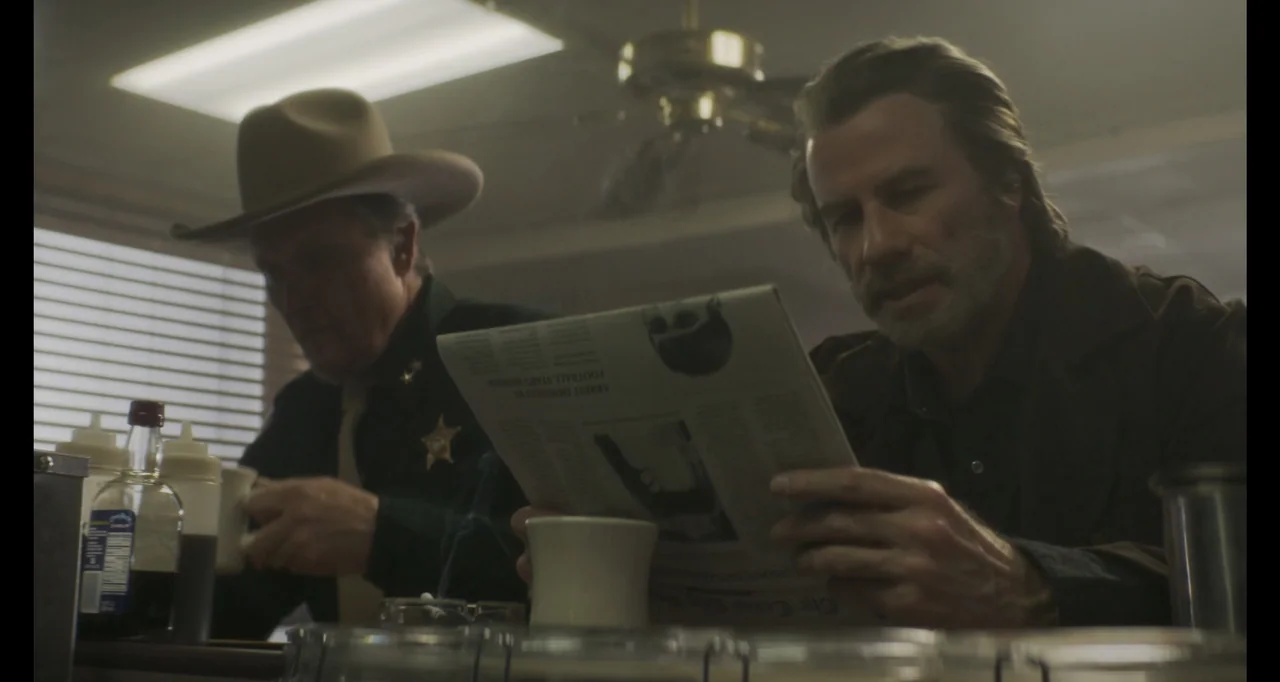 The Poison Rose (2019) movie still: medium — A dimly lit diner booth features wood surfaces and venetian blinds partially covering windows. Two men…