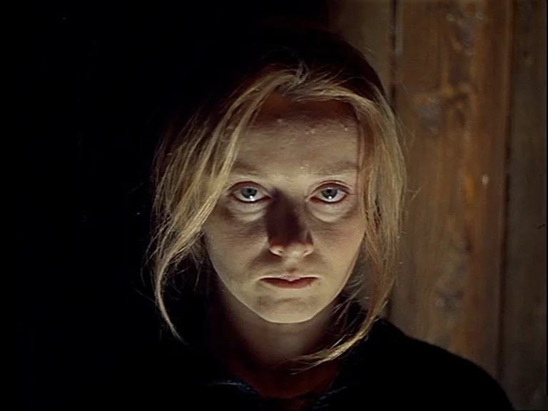 Mirror (Зеркало, Zerkalo) (1975) movie still: closeup — A dimly lit interior space with a wooden surface visible behind the subject. A young woman…