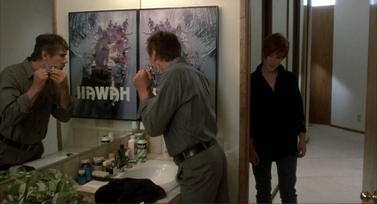 Murphy's Law (2009) movie still: medium — A residential bathroom features a large mirror reflecting a man shaving at the sink. A young person stands…