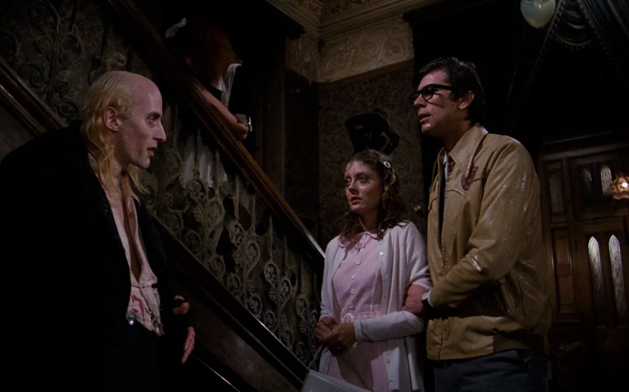 The Rocky Horror Picture Show (1975) movie still: medium — An ornate dark wood foyer features complex carved stair railings and patterned vintage…