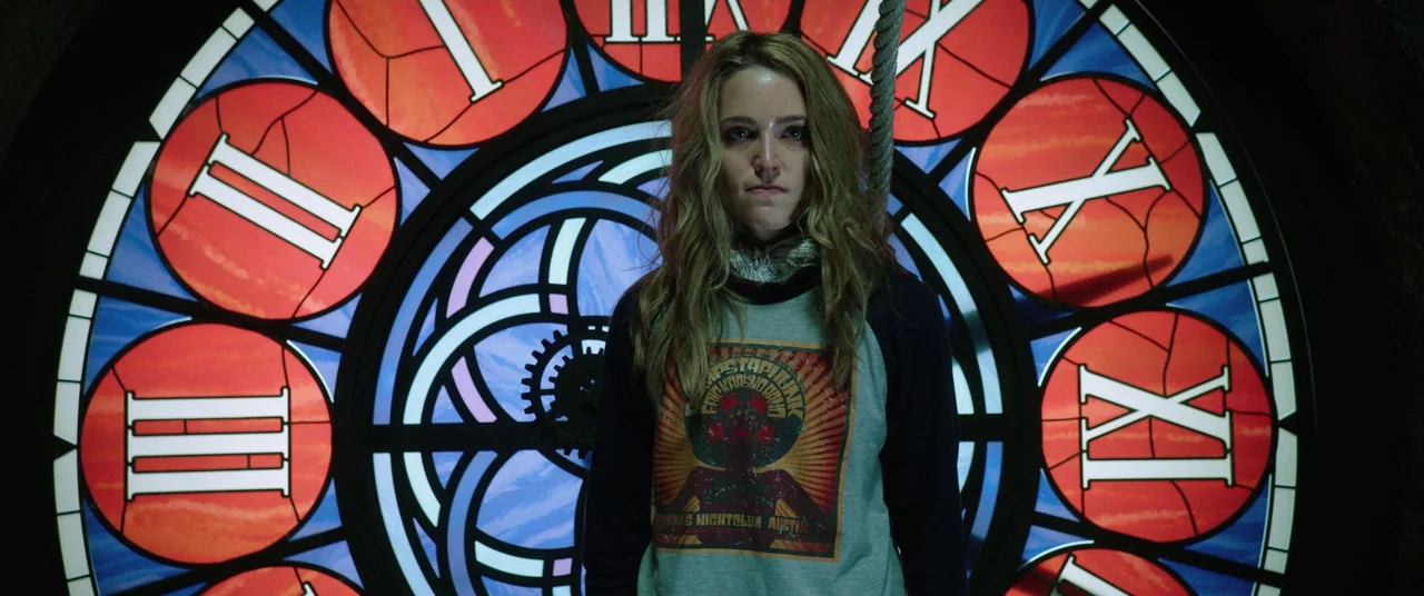 Happy Death Day (2017) movie still: medium — A woman stands before a large backlit circular clock face inside a clock tower. The stained glass…