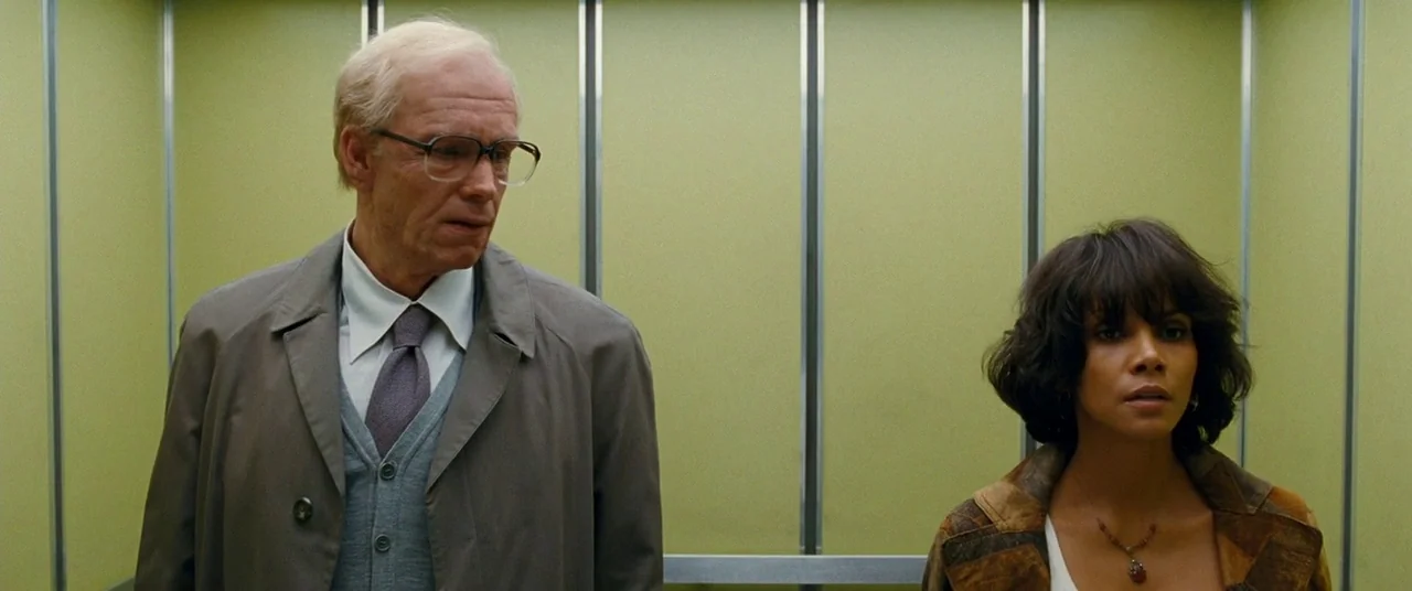 Cloud Atlas (2012) movie still: medium — A modern elevator with light green wall panels and metallic vertical trim. An older man in a trench coat…