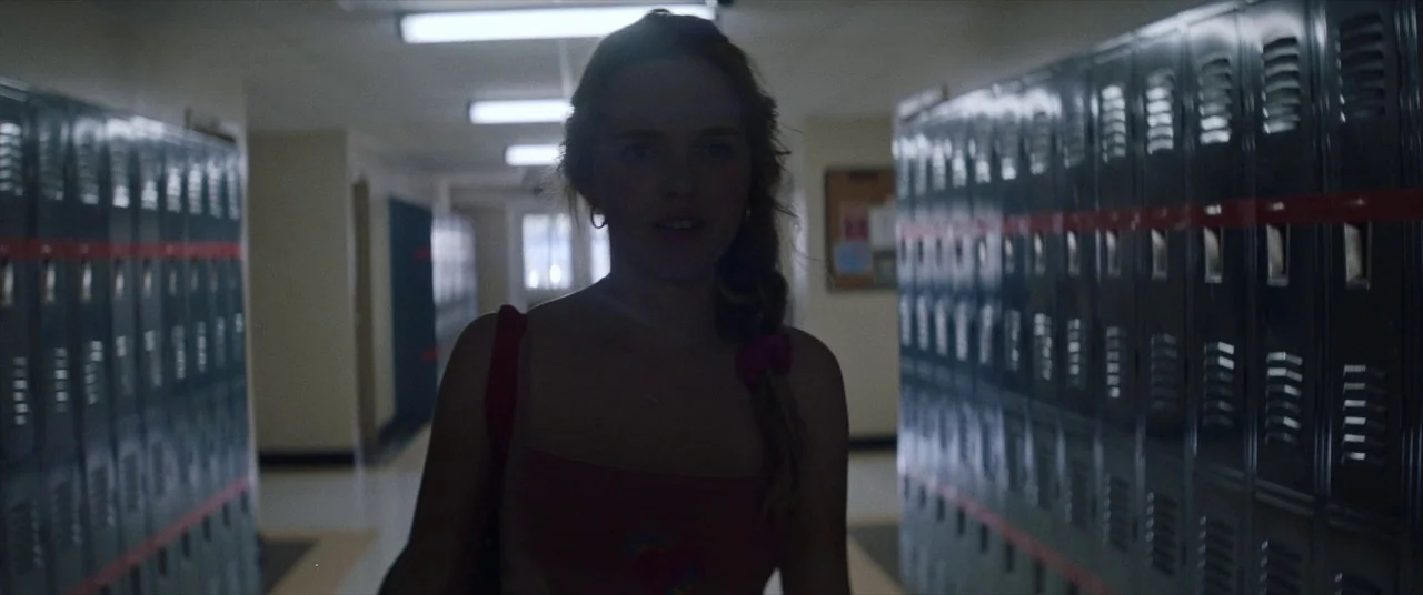 Assassination Nation (2018) movie still: medium — A long, dimly lit institutional corridor lined with metallic grey lockers on both sides. A young…