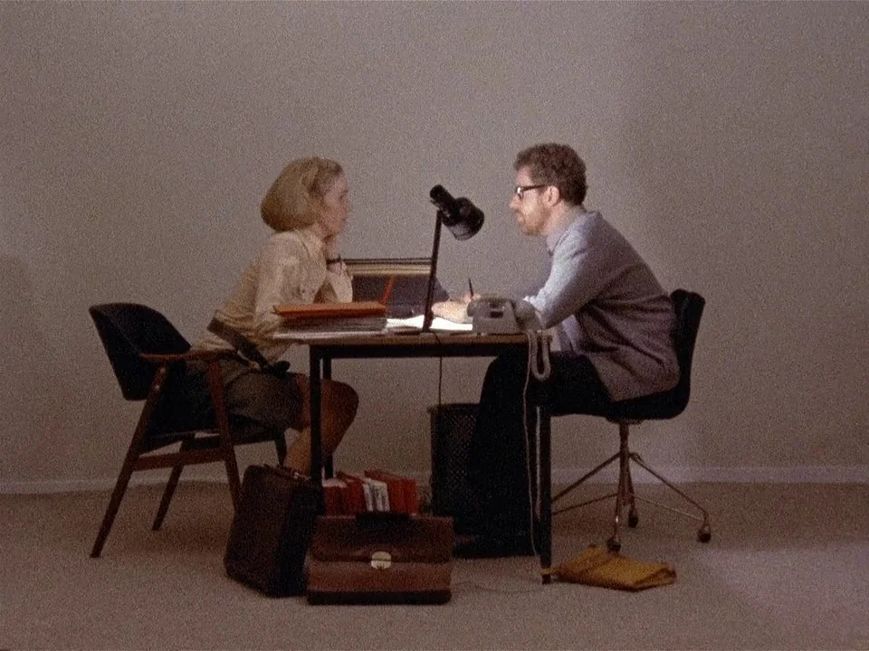 Scenes from a Marriage (1973) movie still: wide — A minimalist office featuring a metal desk, two chairs, and various leather briefcases. A man and…
