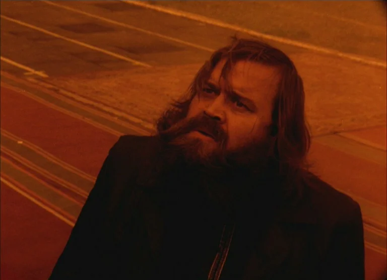 Russian Symphony (1994) movie still: medium — A man stands on a dimly lit track or runway surface. He is positioned at a low angle while tilting his…
