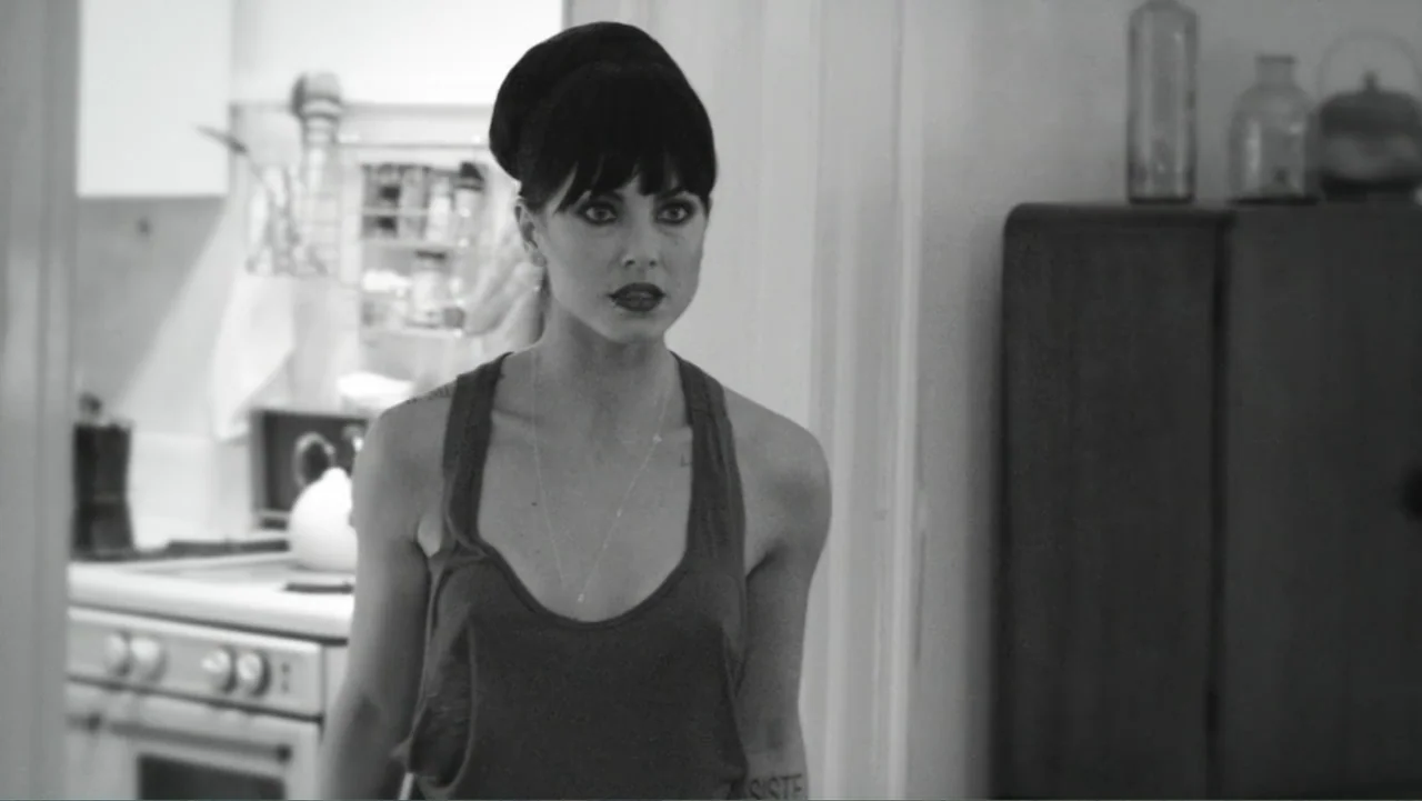 Alice in Marialand (2014) movie still: medium — A woman stands in the doorway of a brightly lit residential space. She gazes slightly off-screen…
