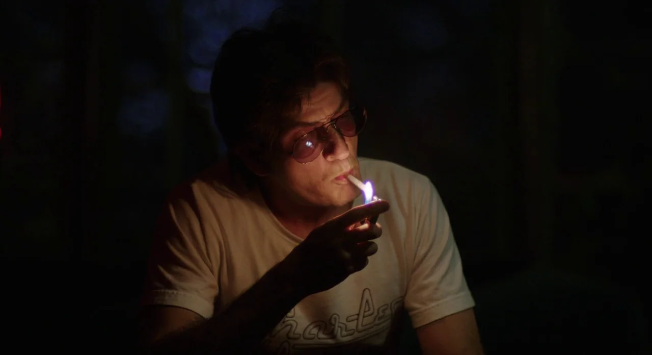 A Glimpse Inside The Mind Of Charles Swan III (2013) movie still: medium — An individual sits outdoors at night in darkness. They hold a lit lighter…