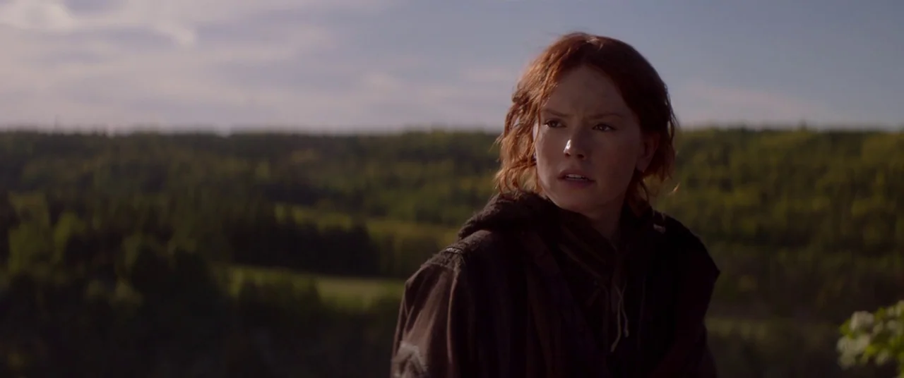 Ophelia (2018) movie still: medium — A woman stands on a hillside overlooking a distant forest under an overcast sky. She looks toward the right…