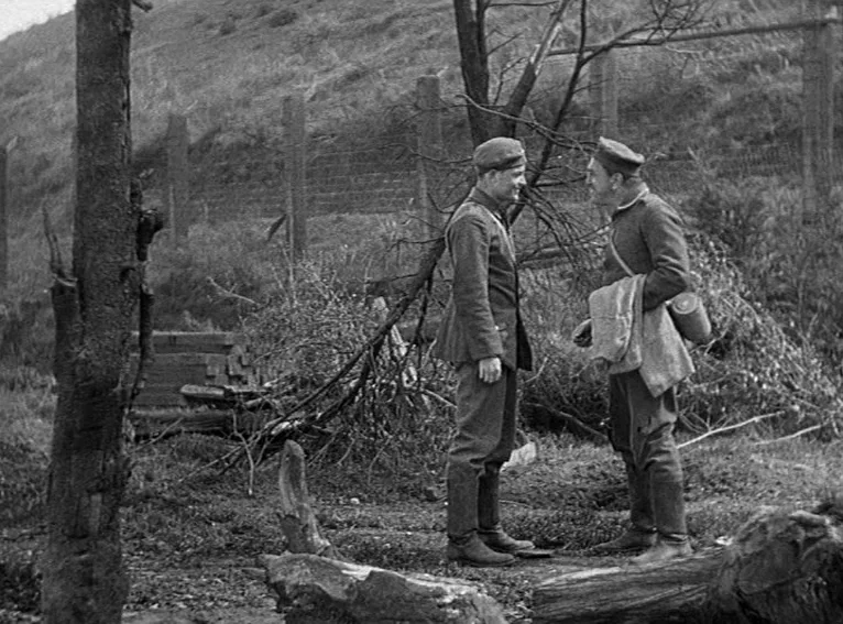 All Quiet on the Western Front (1930) movie still: fullbody — A desolate field features scattered logs, leafless trees, and a distant wire fence.…