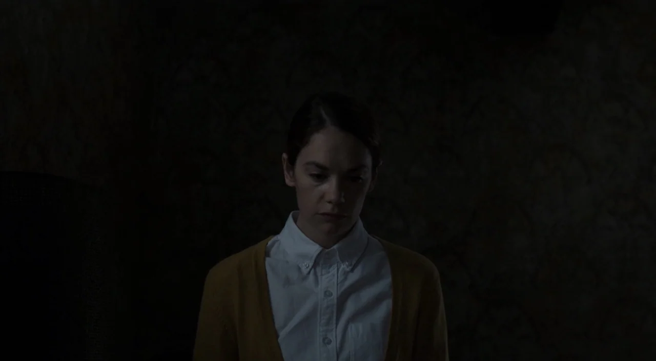 I Am The Pretty Thing That Lives In The House (2016) movie still: medium — A dark room with patterned wallpaper visible in the deep shadows behind a…