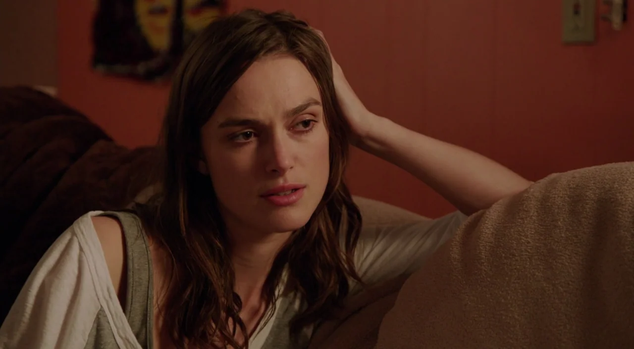 Laggies (2014) movie still: closeup — A residential room has reddish-brown walls and a textured sofa. A woman rests her head on her hand while…