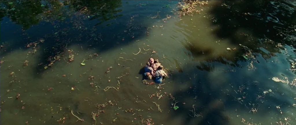Shutter Island (2010) movie still: wide — A dark, murky pond is filled with floating plant debris and lily pads. A cluster of people are visible in…