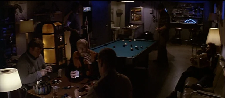 The Thing (1982) movie still: wide — A basement game room contains a card table, a pool table, and a jukebox. Several men gather in the dimly lit…