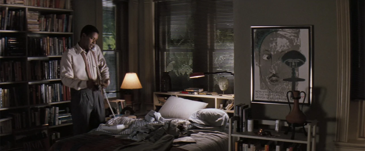 The Pelican Brief (1993) movie still: medium — A cluttered bedroom features a large bookshelf and a framed poster on the wall. A man in a dress…