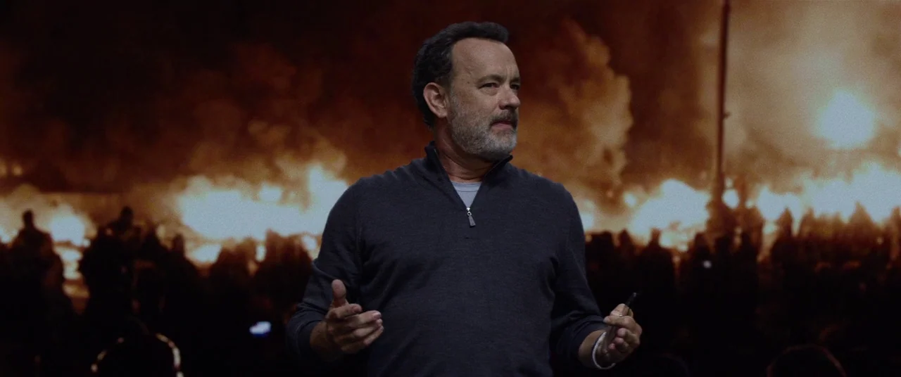 The Circle (2017) movie still: medium — A man stands on a dark stage in front of a massive glowing fire backdrop. He gestures with his hands while…
