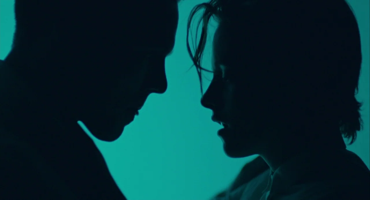 Equals (2015) movie still: closeup — Two human silhouettes face each other against a solid, vibrant cyan light source. The figures occupy the sides…