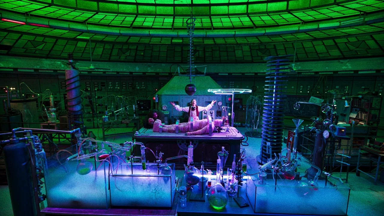 The Munsters (2022) movie still: wide — A subterranean laboratory features curved ceilings and rows of vintage scientific equipment. A scientist…