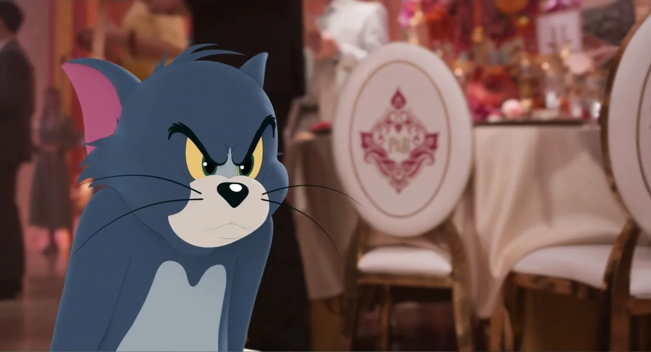 Tom & Jerry (2021) movie still: closeup — A decorated indoor event space with blurry banquet tables in the background. The animated cat Tom is…