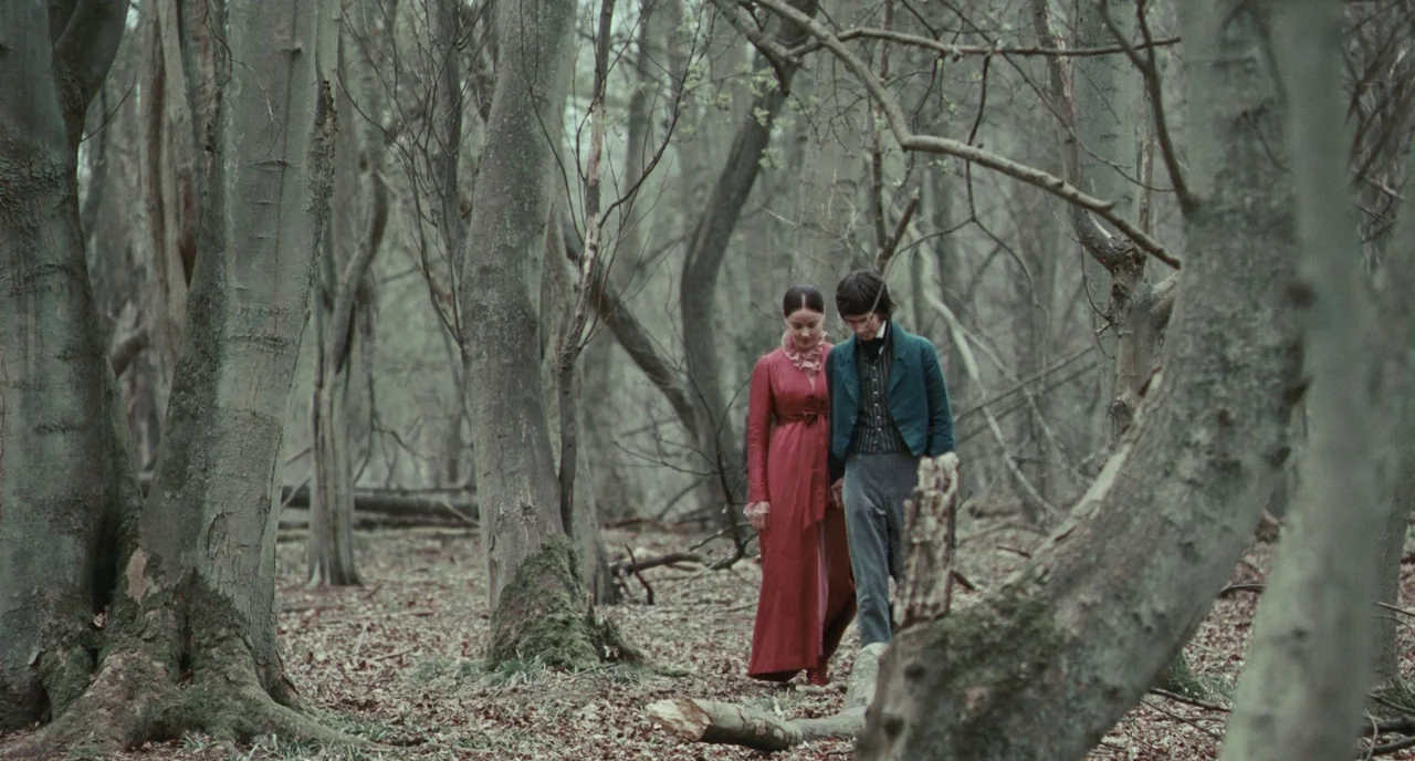 Bright Star (2009) movie still: fullbody — A dense, leafless woodland with mossy tree trunks and a ground covered in dead leaves. A man and a woman…