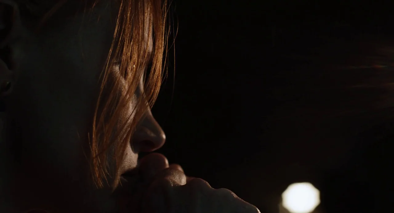 Zero Dark Thirty (2012) movie still: closeup — A woman stands in a pitch black environment with only her face partially illuminated. She holds her…