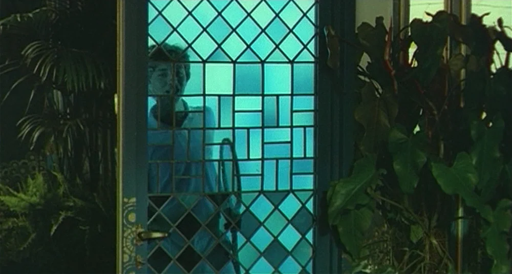 Footprints (Le Orme) (1975) movie still: medium — A residential entrance features a dark door with geometric grid glass panels. A man stands behind…