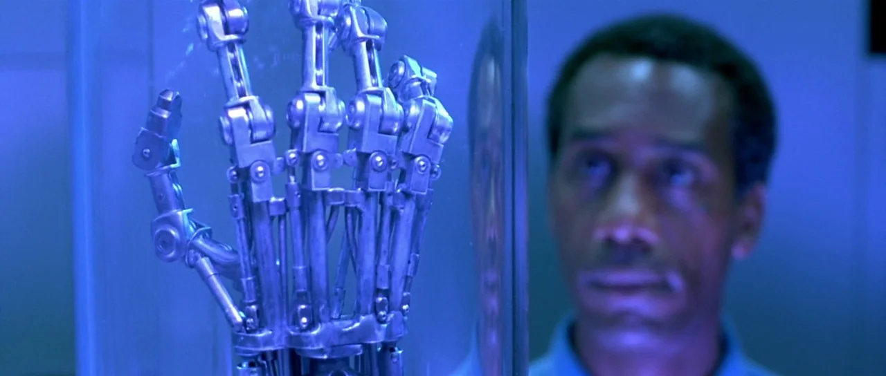 Terminator 2: Judgement Day (1991) movie still: medium — A laboratory setting features a metallic robotic hand displayed inside a clear glass case.…