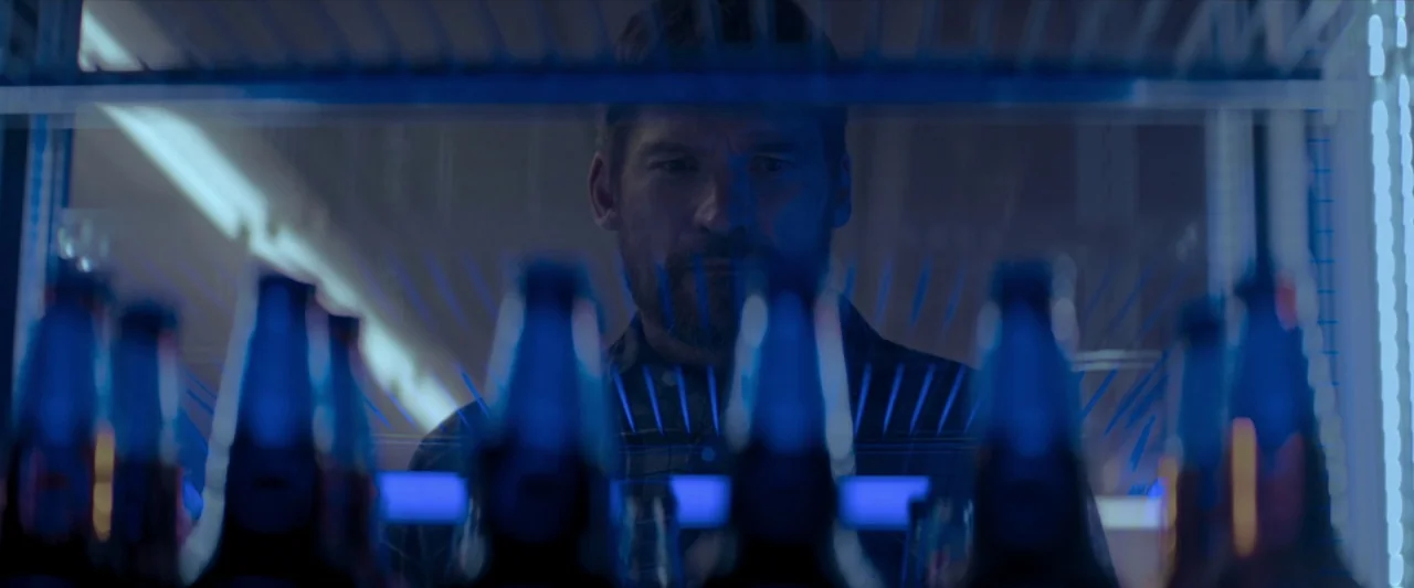 The Silencing (2020) movie still: closeup — A man stands in front of a glass display case filled with rows of bottles. He peers through the clear…